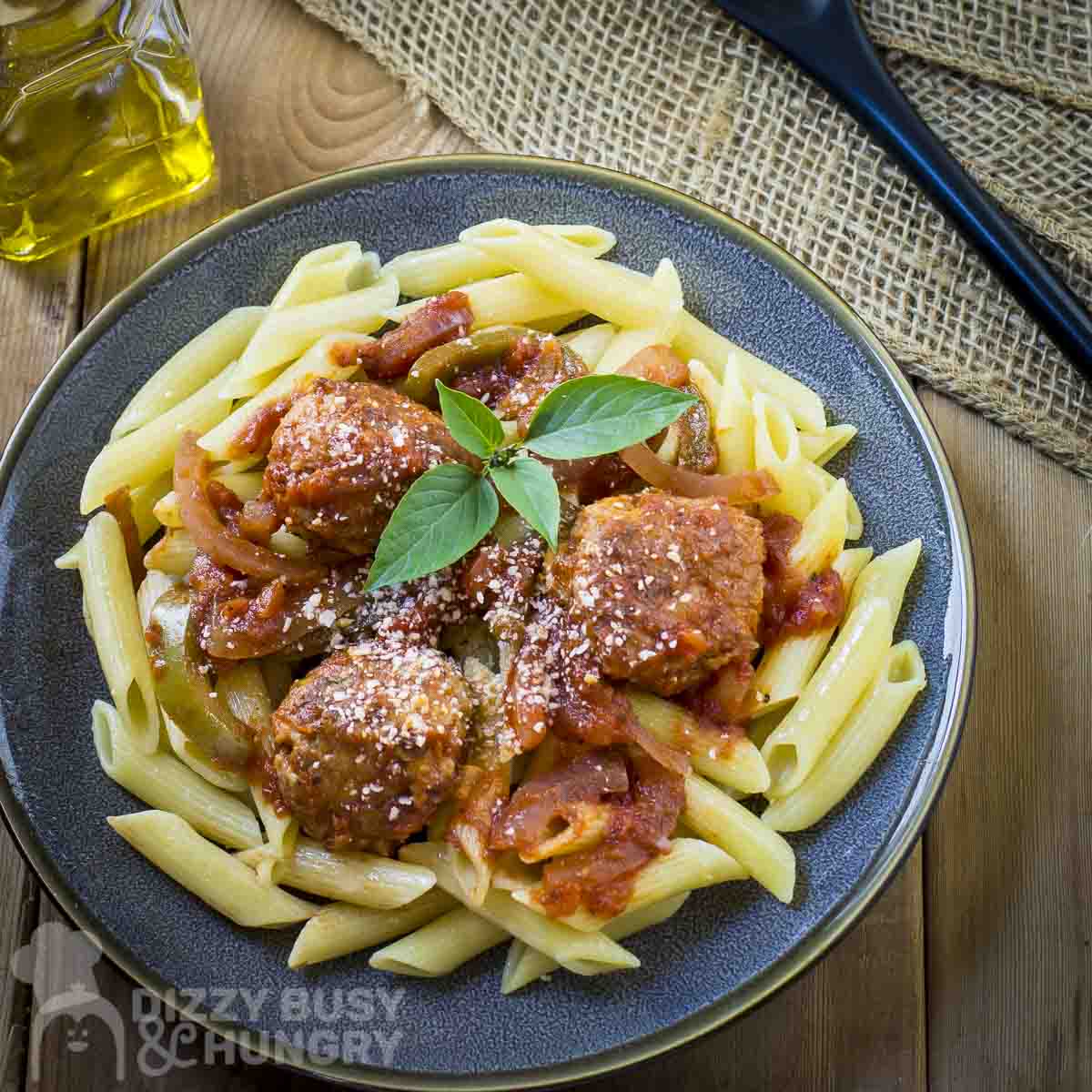 Overhead shot of meatballs and sauce over a bed of penne garnished with fresh basil on a black plate.