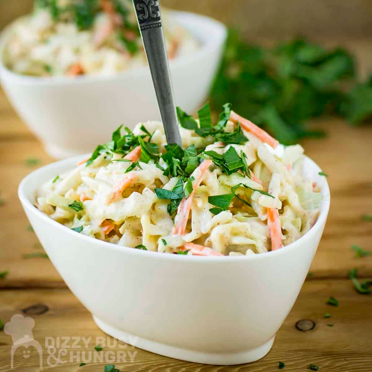 Side shot of a white bowl with chipotle coleslaw garnished with fresh herbs on a wooden table.