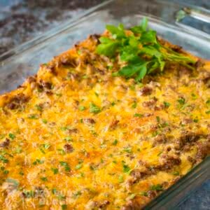 Side shot of crescent roll casserole in a baking dish garnished with fresh herbs on a marble countertop.