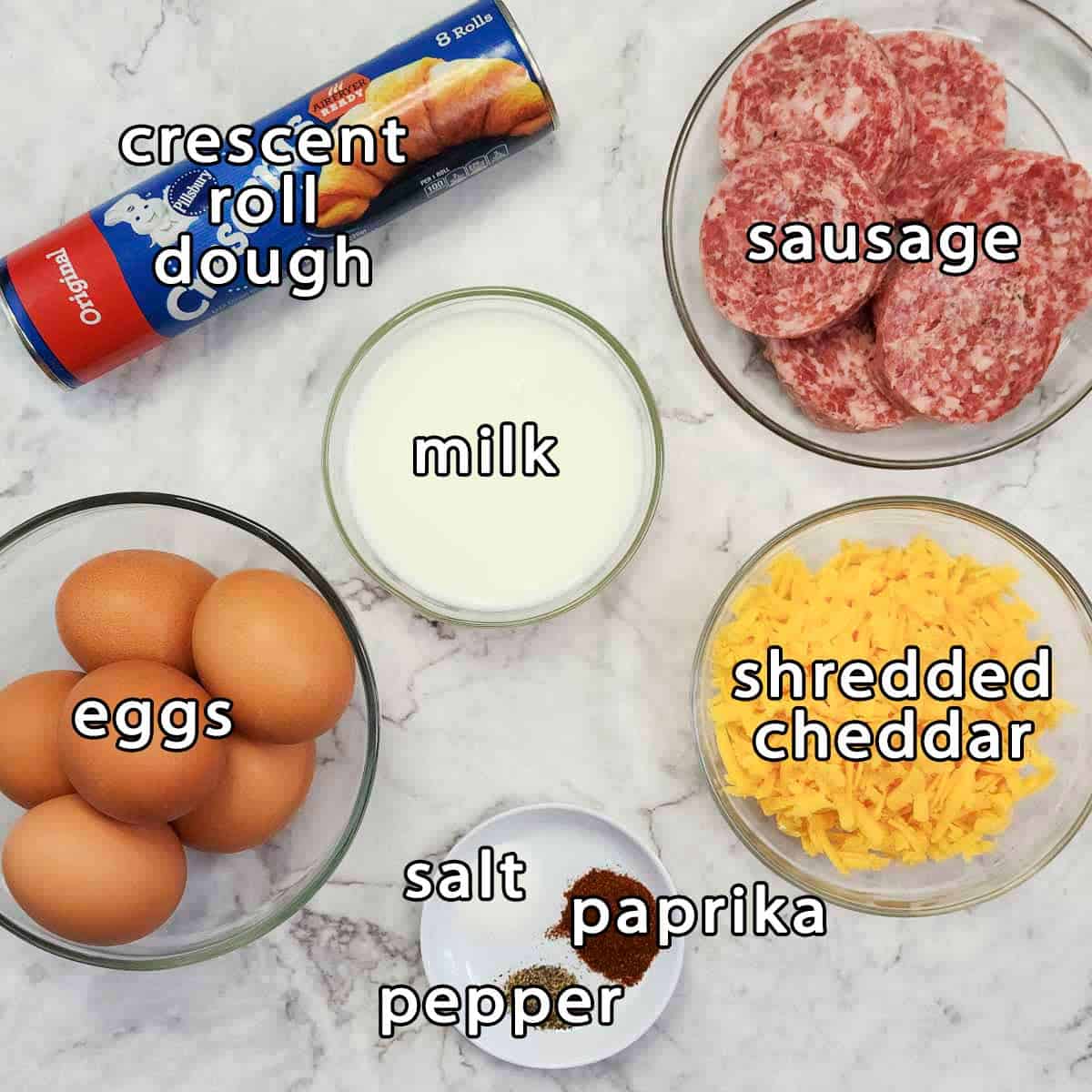 Overhead shot of ingredients - crescent roll dough, milk, sausage, eggs, shredded cheddar, salt, paprika, and pepper.