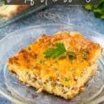 Side shot of a piece of crescent roll casserole on a clear plate with a black fork on the side with a full baking dish of the casserole and fresh herbs in the background.