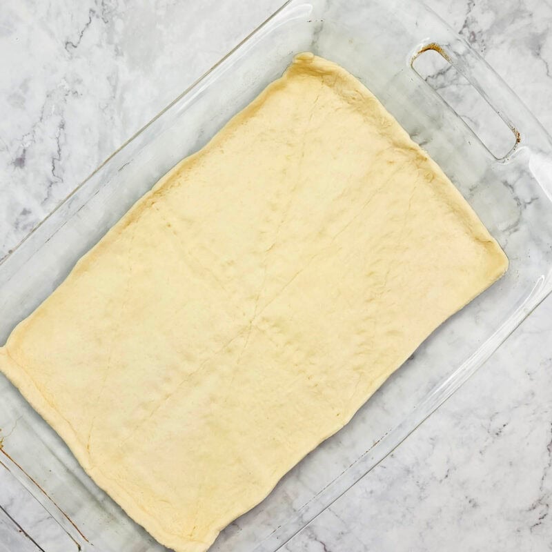 Overhead view of process shot 2 - unroll the crescent dough and press it into the bottom of the baking dish, pinching the seams together to form a crust.