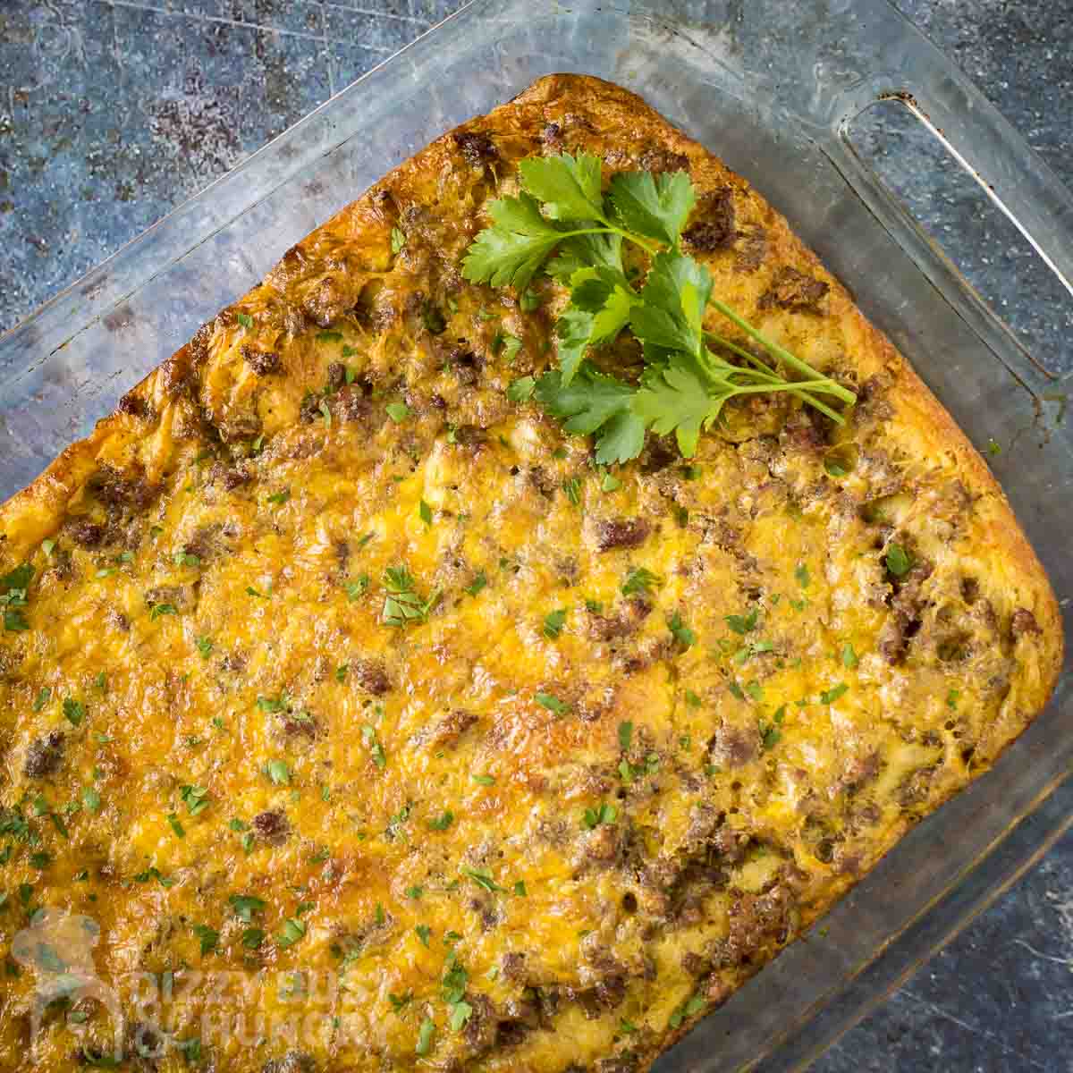 Overhead shot of crescent roll casserole in a baking dish garnished with fresh herbs on a marble countertop.