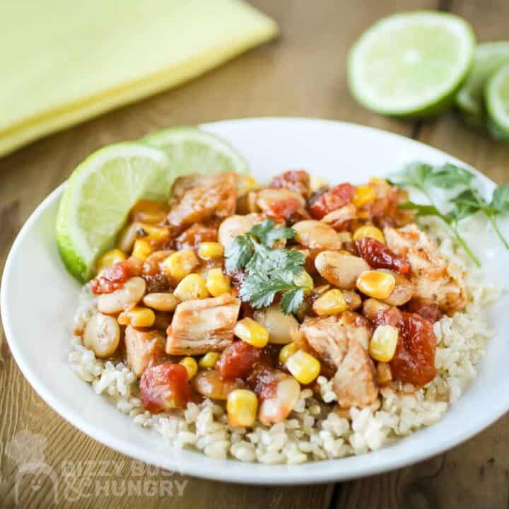 Side shot of mango salsa chicken and butter beans over rice garnished with fresh herbs and lime slices in a white bowl.