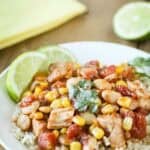 Side shot of mango salsa chicken and butter beans over rice garnished with fresh herbs and lime slices in a white bowl.
