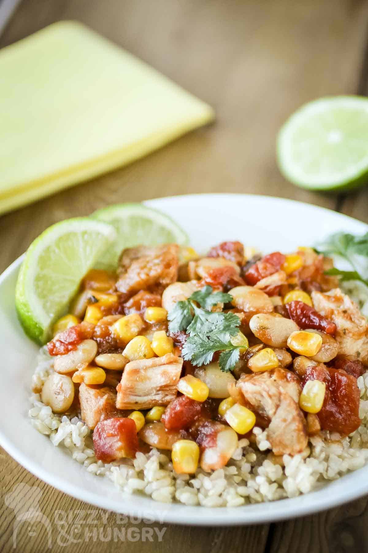 Side shot of mango salsa chicken and butter beans over rice garnished with fresh herbs and lime slices in a white bowl.