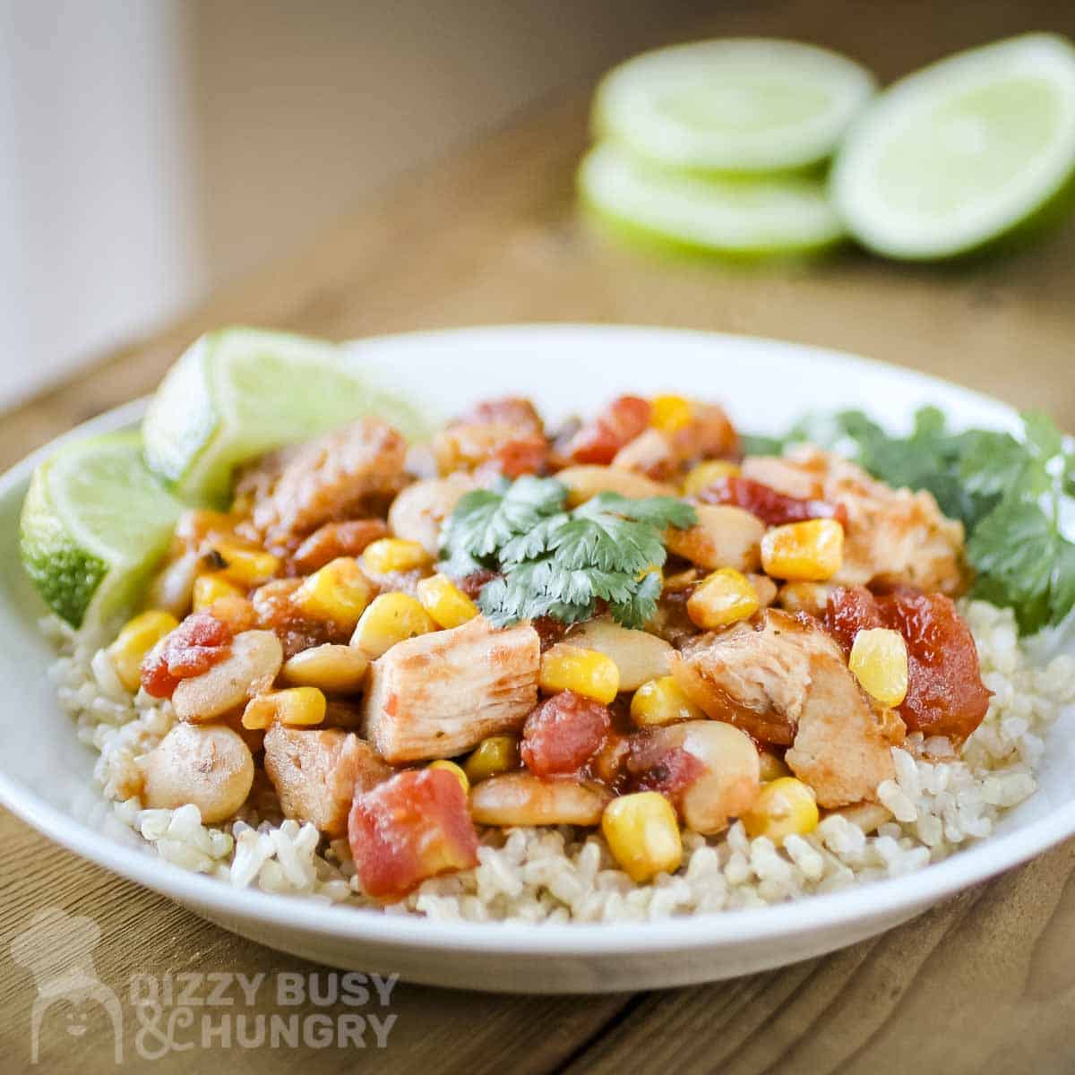 Side shot of mango salsa chicken and butter beans over rice garnished with fresh herbs and lime slices in a white bowl.