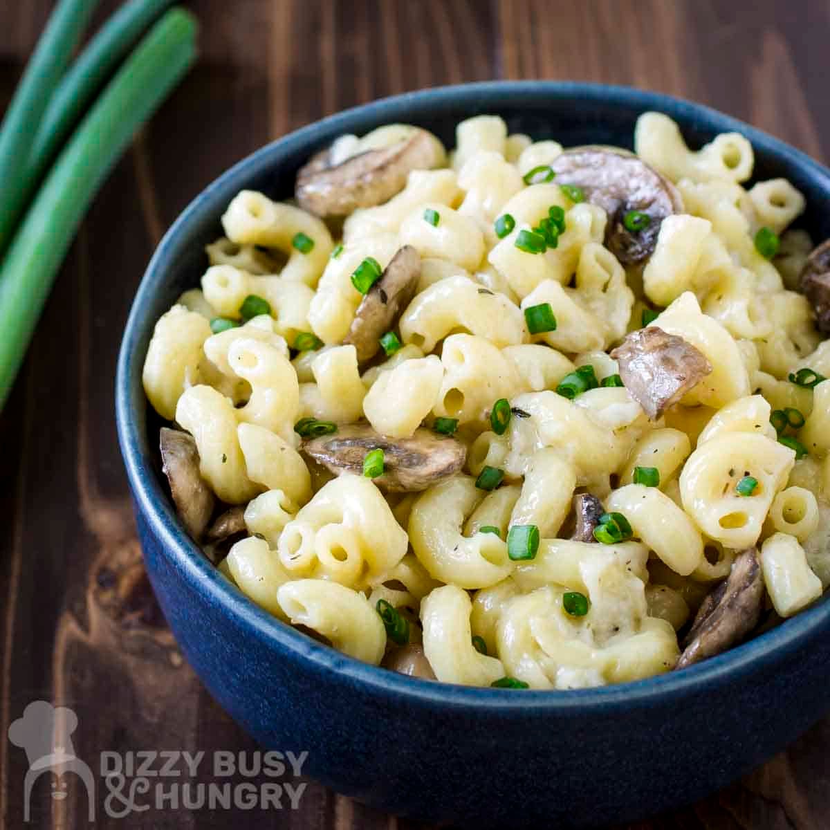 Side shot of mushroom mac and cheese garnished with fresh green onions slices in a blue bowl.