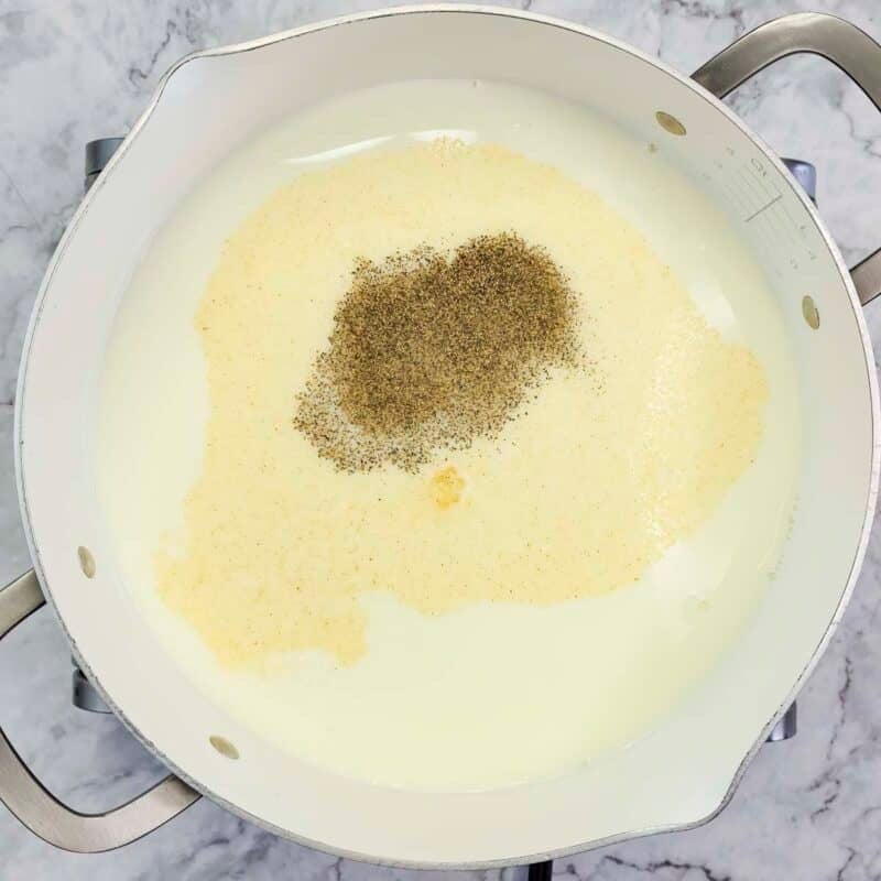 Overhead view of process shot 2 - in a large pot over medium high heat, add the milk, water, garlic powder, salt, and pepper. Bring to a gentle simmer.