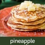Side shot of a stack of pineapple pancakes garnished with coconut shreds and pineapple chunks on an orange plate.