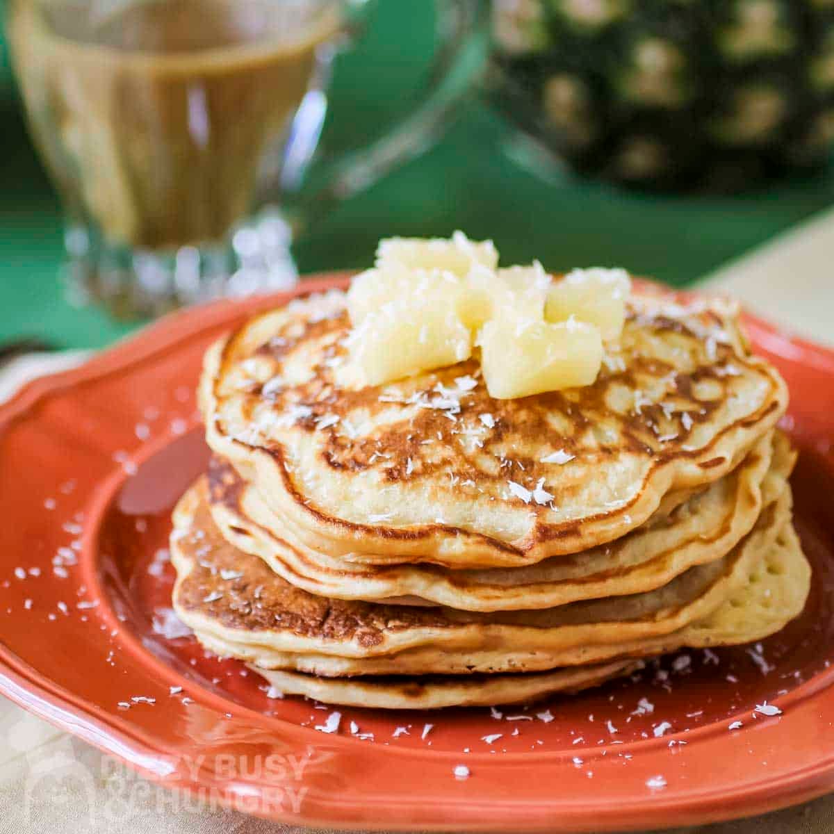 Side shot of a stack of pineapple pancakes garnished with coconut shreds and pineapple chunks.
