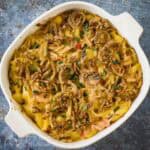 Overhead shot of seafood mac and cheese garnished with french fried onions and fresh herbs in a white baking dish.