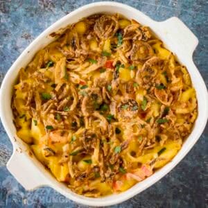 Overhead shot of seafood mac and cheese garnished with french fried onions and fresh herbs in a white baking dish.