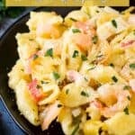 Side shot of seafood mac and cheese garnished with fresh herbs on a black plate with more fresh herbs in the background.