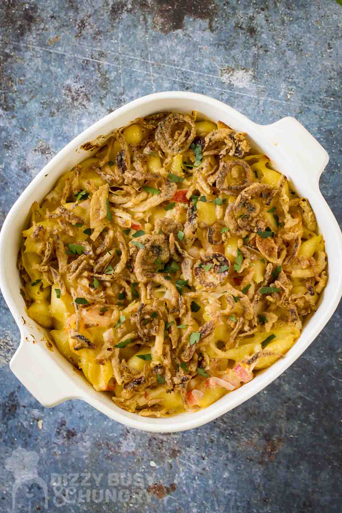Overhead shot of seafood mac and cheese garnished with french fried onions and fresh herbs in a white baking dish.