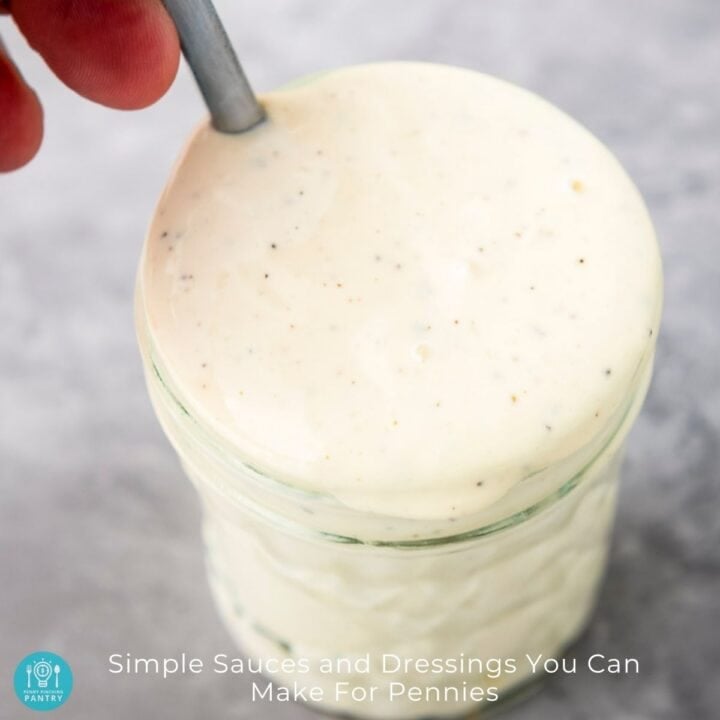 Overhead view of homemade dressing in a medium mason jar with a hand stirring a spoon in it.