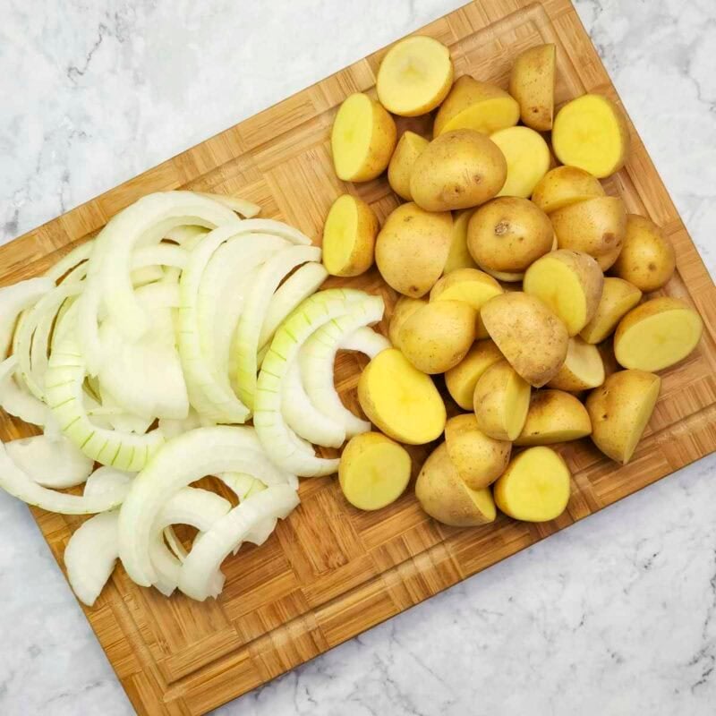 Overhead view of process shot 1 - peel and slice the onion. Wash the baby potatoes and cut them in half.