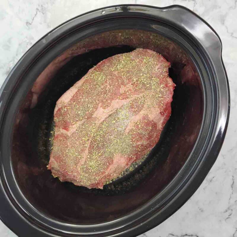 Overhead view of process shot 2 - place the roast in the slow cooker and season it with the salt, pepper, and italian seasoning.