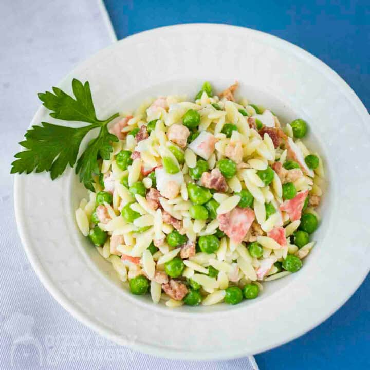 Overhead shot of crab pasta salad in a white bowl garnished with fresh parsley.