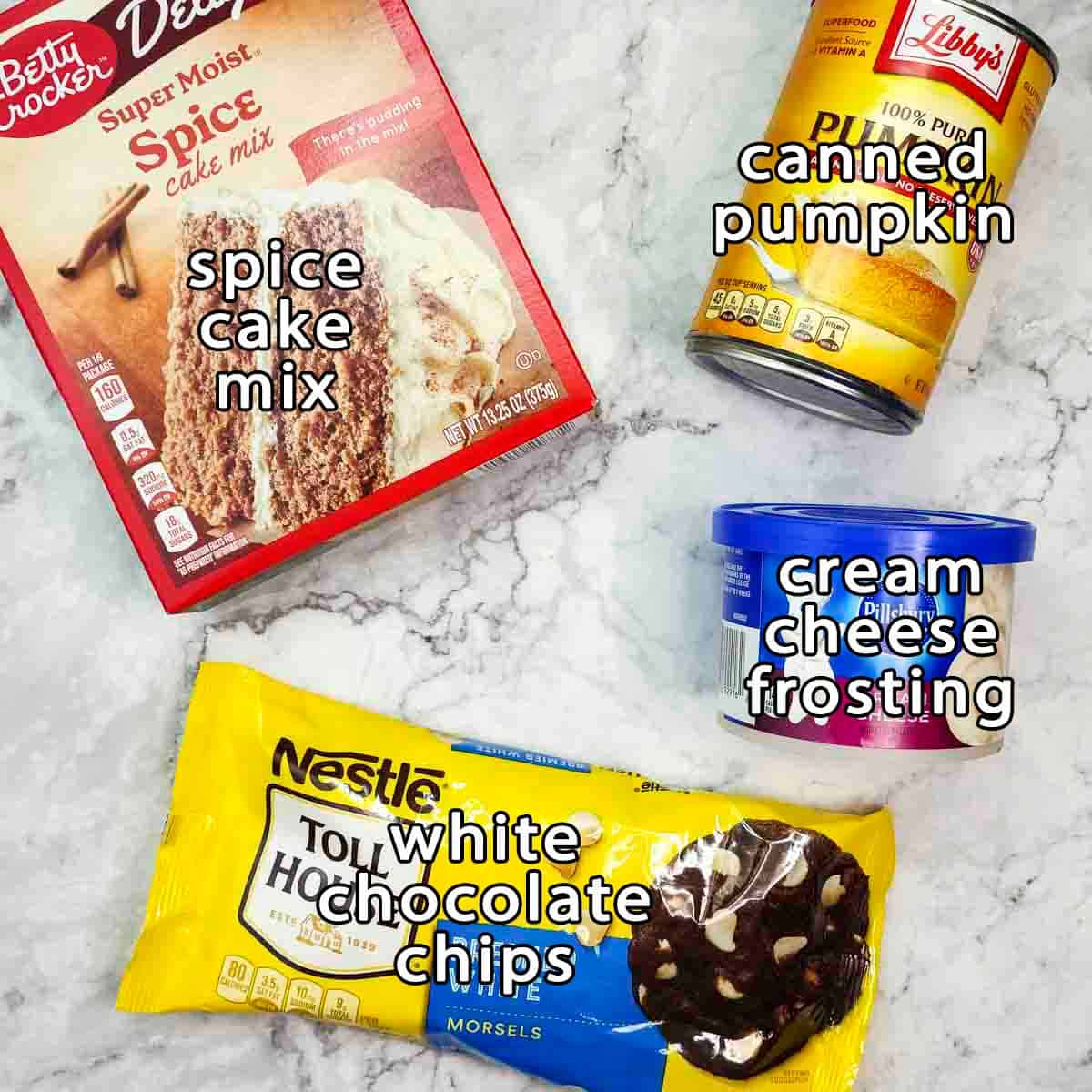Overhead shot of ingredients - spice cake mix, canned pumpkin, cream cheese frosting, white chocolate chips, and canned pumpkin.