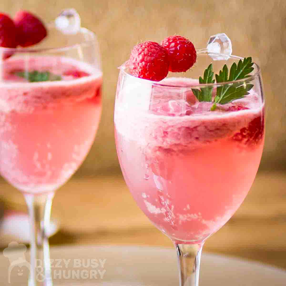 Side shot of two cocktail glasses with raspbery spritz garnished with fresh mint and raspberries.