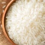 Top down view of a bowl of uncooked rice resting on a piece of burlap.