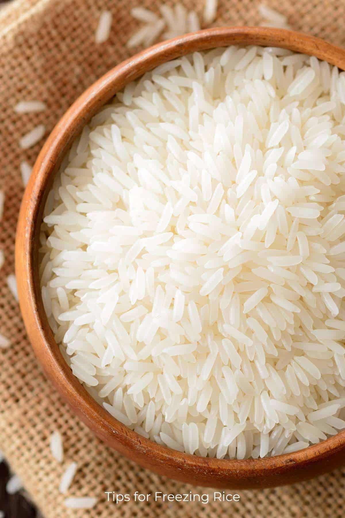 Top down view of a bowl of uncooked rice resting on a piece of burlap.