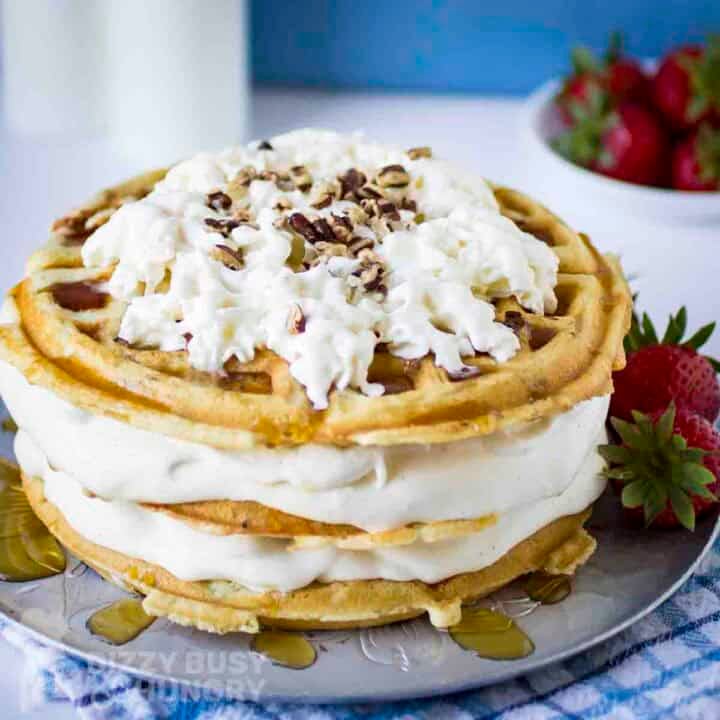 Side shot of waffle ice cream cake garnished with whipped cream and chopped nuts on a grey plate with strawberries on the side.