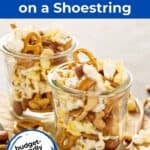 Trail mix including popcorn, pretzels, and peanuts in a glass jar sitting on a piece of brown parchment paper.