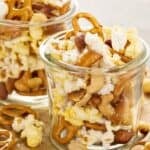 Trail mix including popcorn, pretzels, and peanuts in a glass jar as an example of cheap snacks.