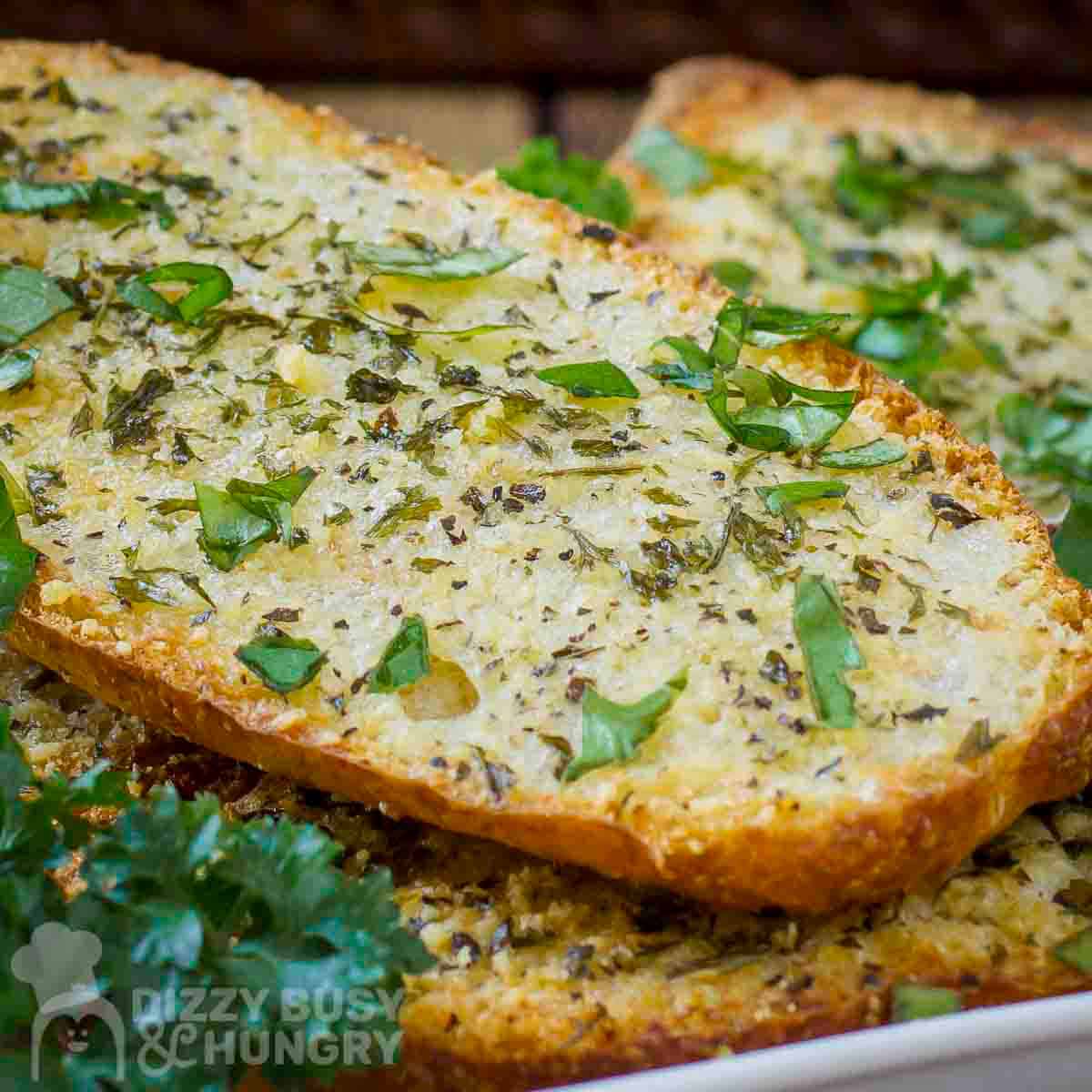 Side shot of multiple slices of garlic bread garnished with fresh herbs on a white plate.