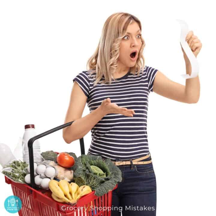 Woman with grocery basket full of food holding a receipt and looking at it with a shocked expression.