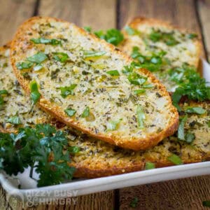 Side shot of multiple slices of garlic bread garnished with fresh herbs on a white plate.