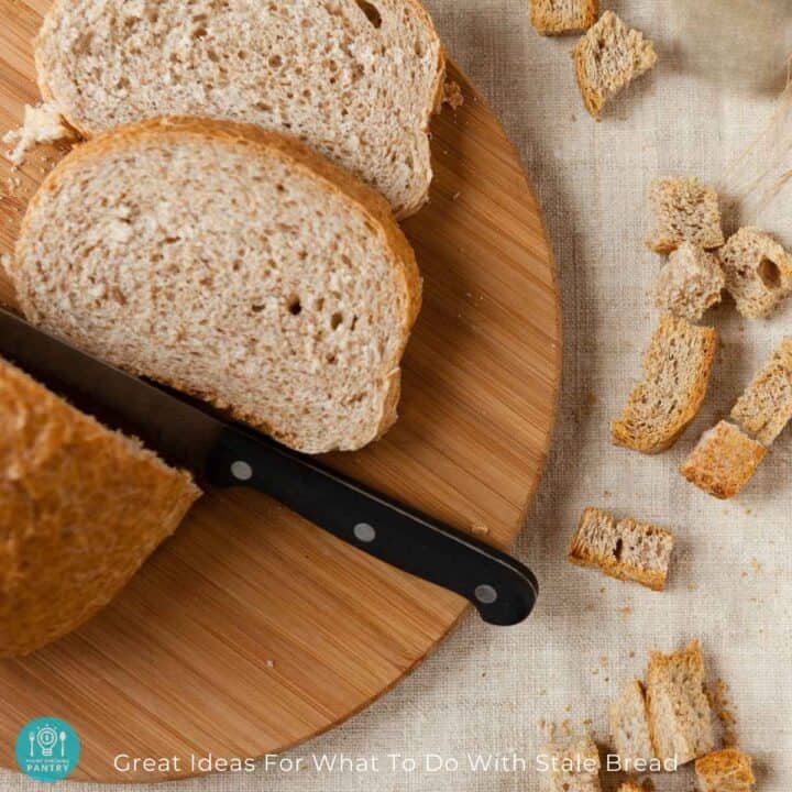 Slices of whole wheat bread with a knife on a cutting board with bread cubes to the right on a cream-colored linen tablecloth.
