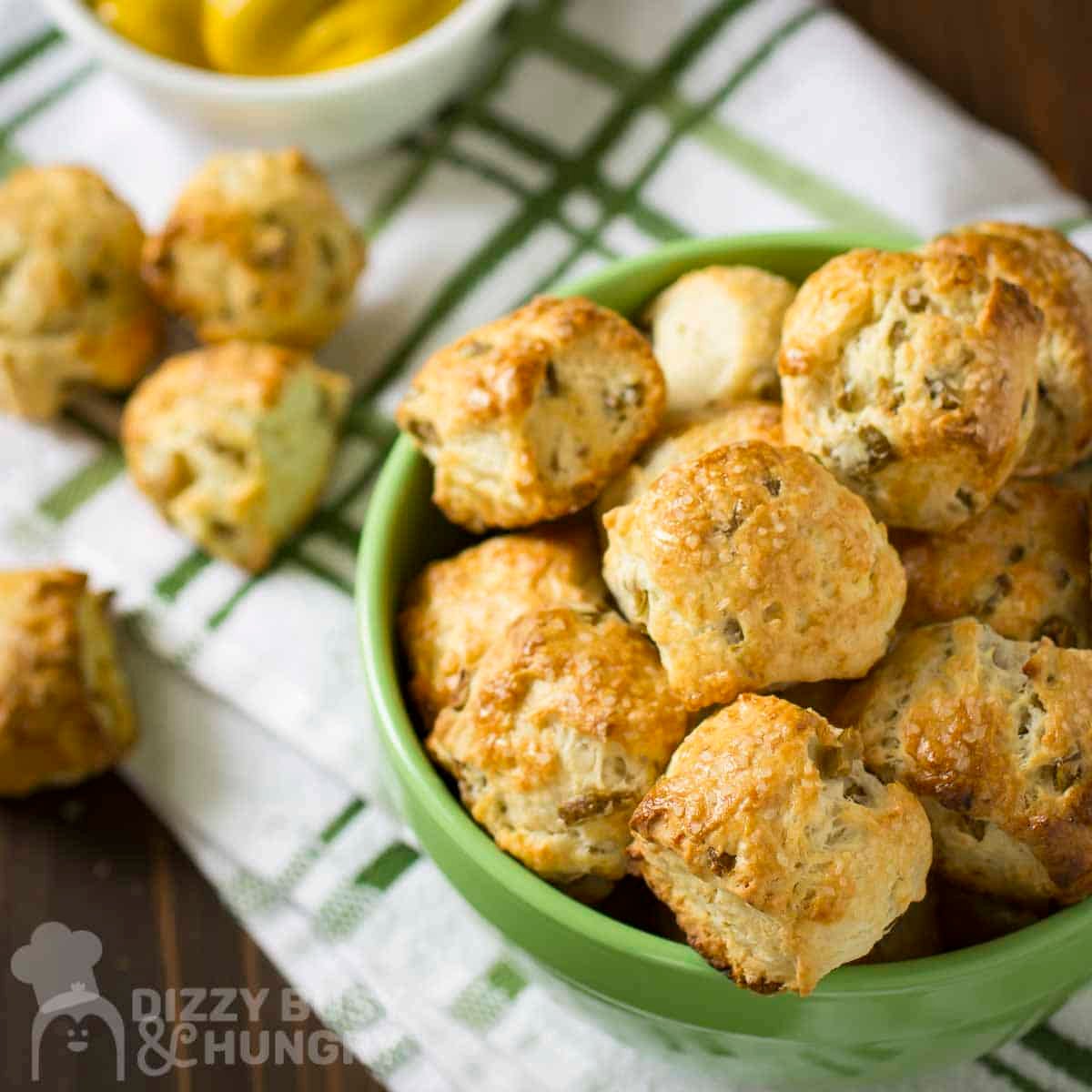 Side angled shot of multiple pretzel nuggets in a green bowl with more on the side and a bowl of lemons in the background.