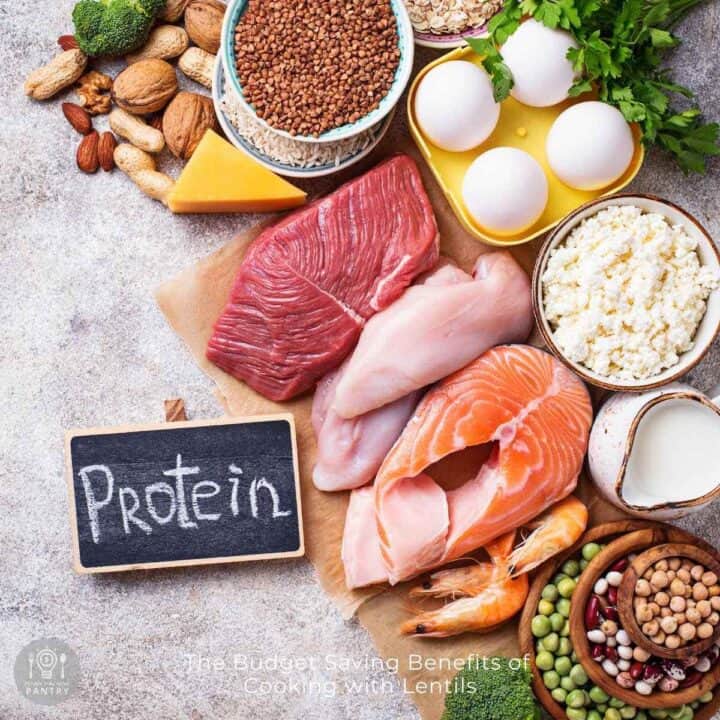 Overhead view of possible cheap protein sources like beans and quinoa on a gray concrete counter with a small chalkboard to the side that has the word 'protein' written on it.