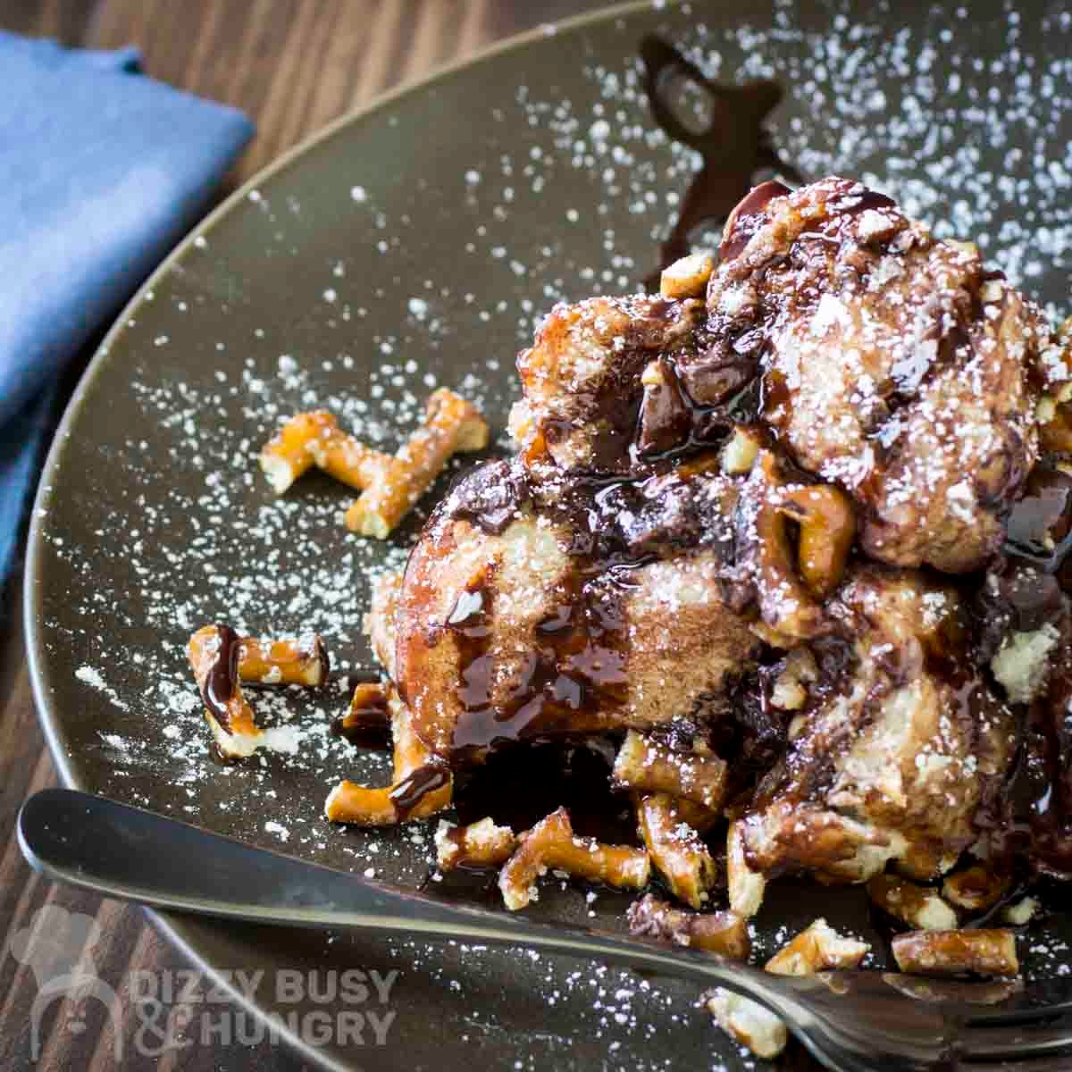 Side shot of a slice of monkey bread sprinkled with powdered sugar on a grey plate with a fork on the side.