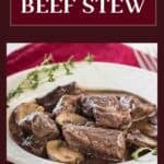 Side shot of beef stew in a white bowl with fresh thyme on the sides all on a red cloth.