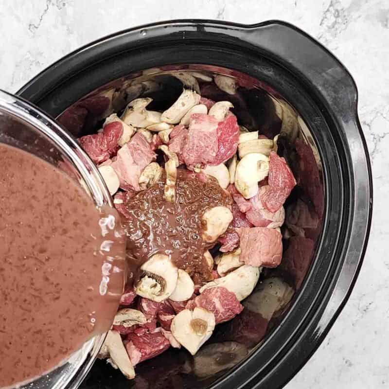 Overhead view of process shot 3 - pour the wine mixture over the beef and mushrooms.