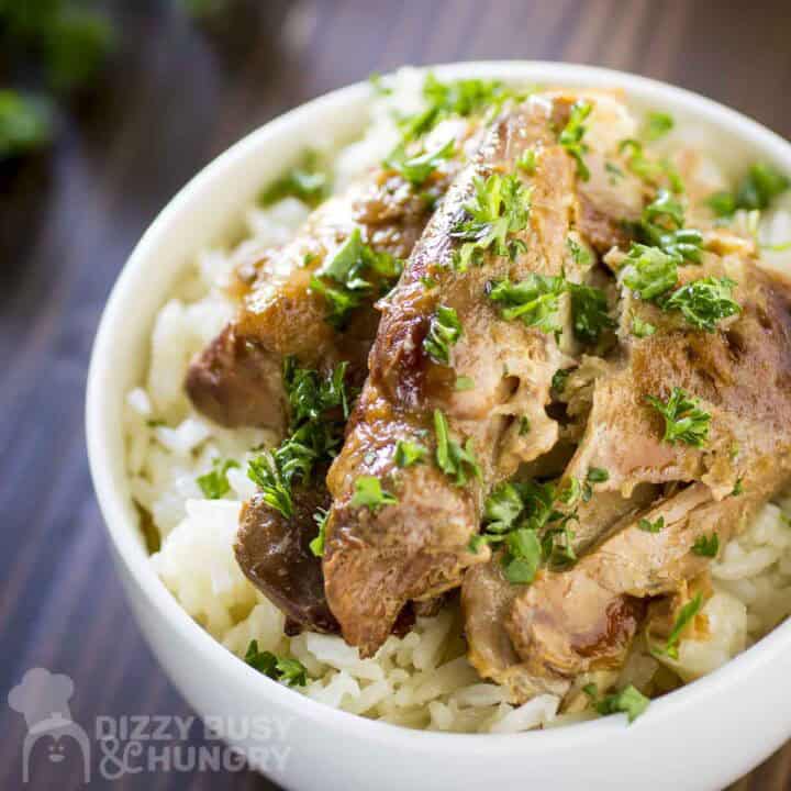 Side close up shot of beer chicken on a bed of rice in a white bowl garnished with fresh herbs.