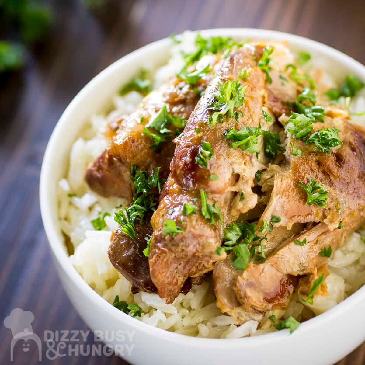 Side close up shot of beer chicken on a bed of rice in a white bowl garnished with fresh herbs.