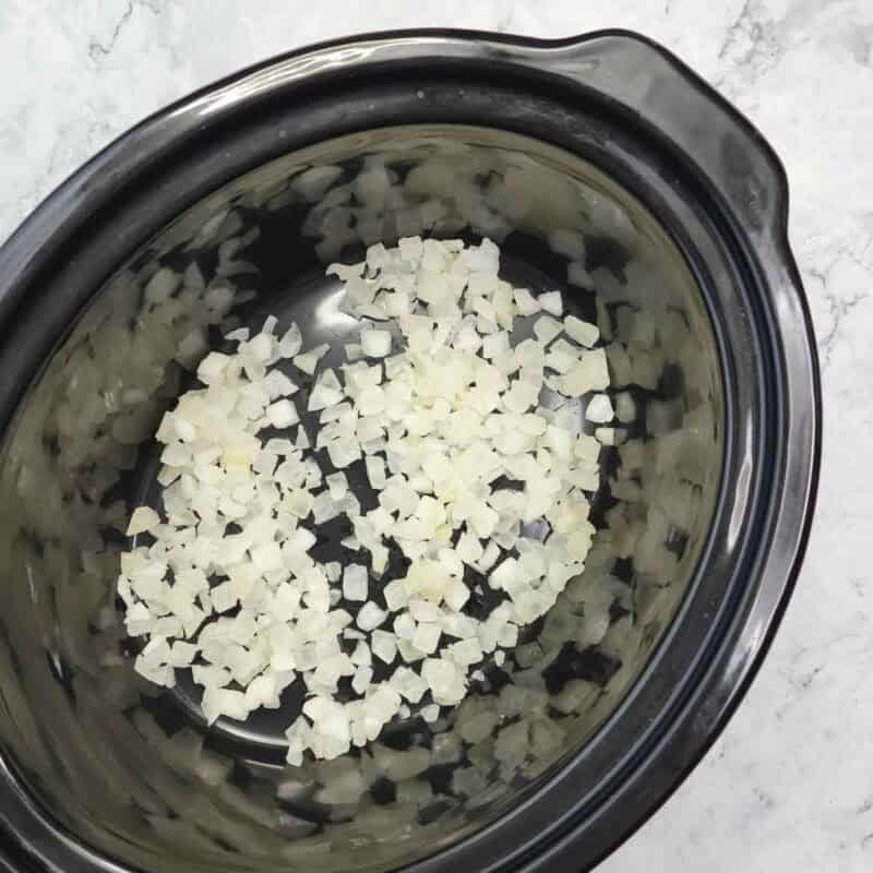 Overhead view of process shot 1 - cover the bottom of the crock pot with the chopped onion.
