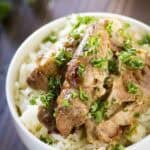 Side close up shot of beer chicken on a bed of rice in a white bowl garnished with fresh herbs.