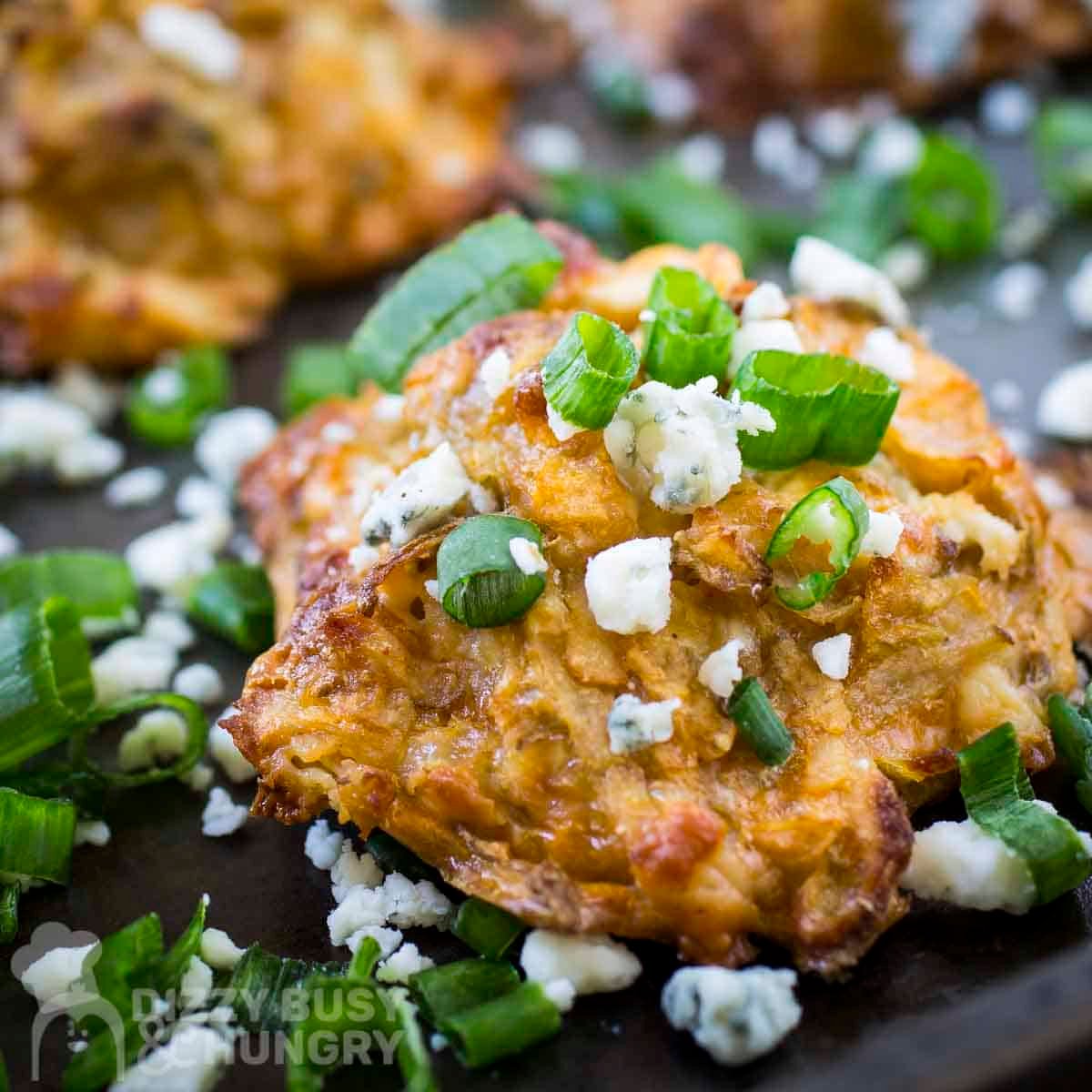 Side close up shot of a potato bite on a baking sheet garnished with blue cheese crumbles and green onions.