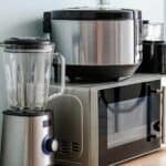 Photo of a blender, microwave, instant pot, and other small kitchen appliances on a wood counter.
