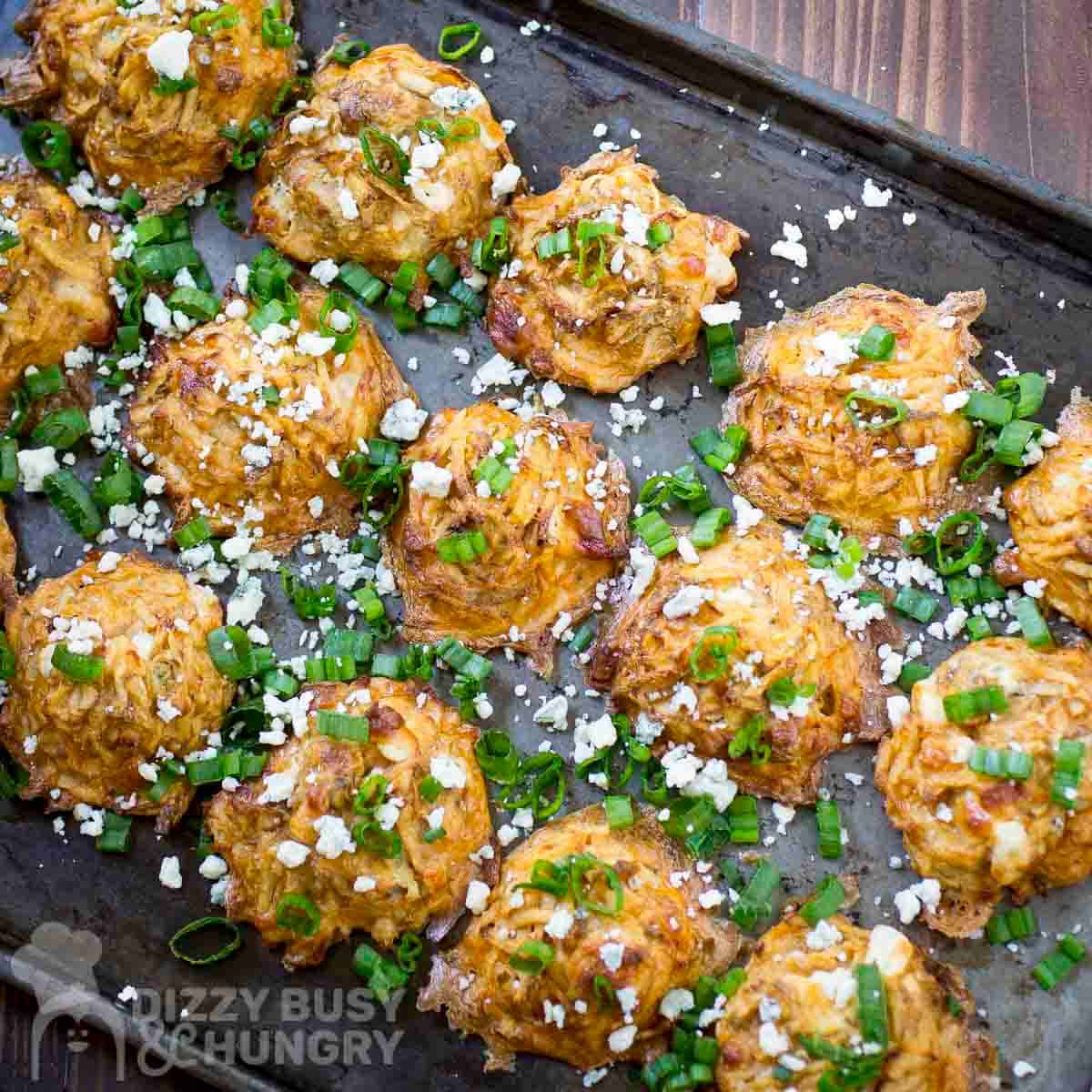 Overhead shot of potato bites on a baking sheet garnished with blue cheese crumbles and green onions