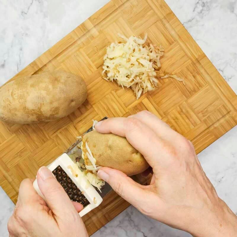 Overhead view of process shot 1 - shred the potatoes to make about 2 cups and squeeze them in a clean towel to remove excess liquid.