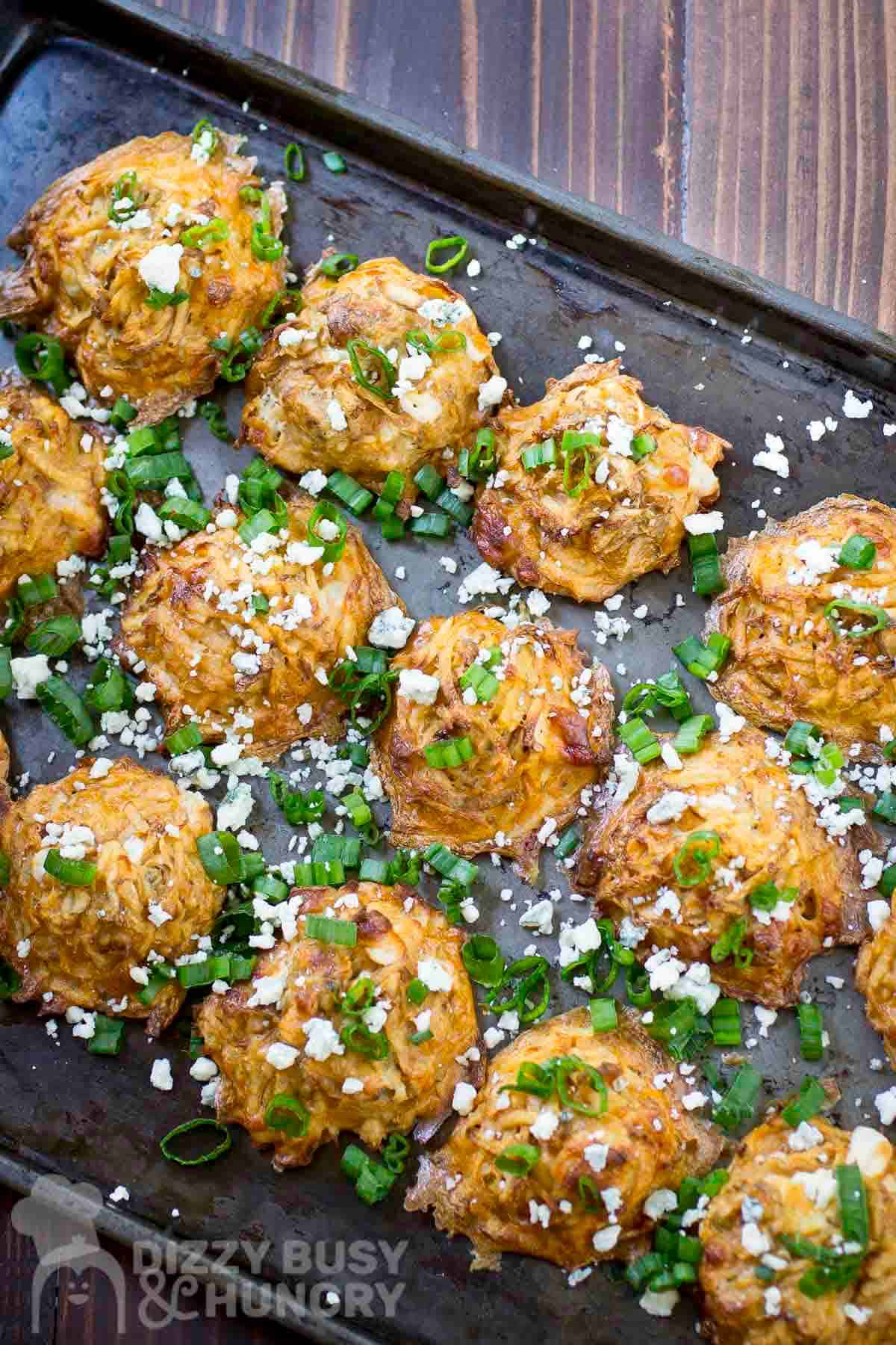 Overhead shot of potato bites on a baking sheet garnished with blue cheese crumbles and green onions.
