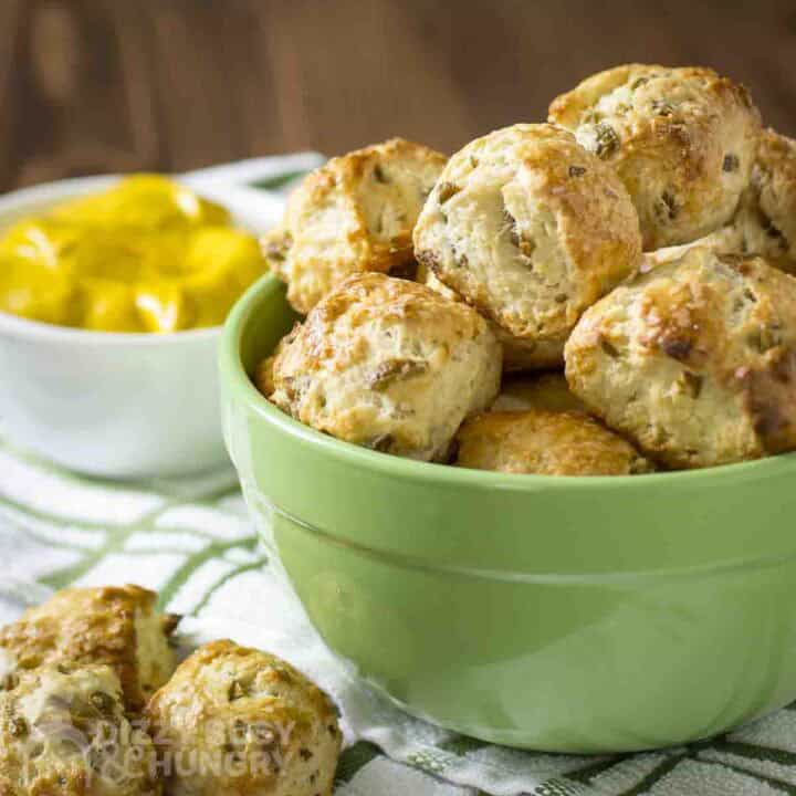 Side shot of multiple pretzel nuggets in a green bowl with more on the side and a bowl of lemons in the background.