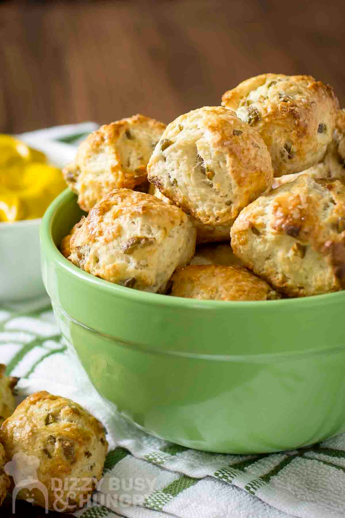 Side shot of multiple pretzel nuggets in a green bowl with more on the side and a bowl of lemons in the background.